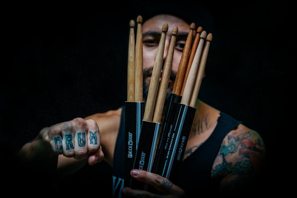 Musician showing drumsticks and tattoos, emphasizing creativity and style.